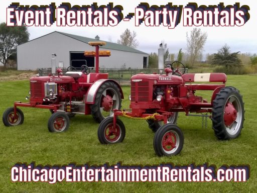 Two vintage red tractors parked on green grass with a barn in the background.