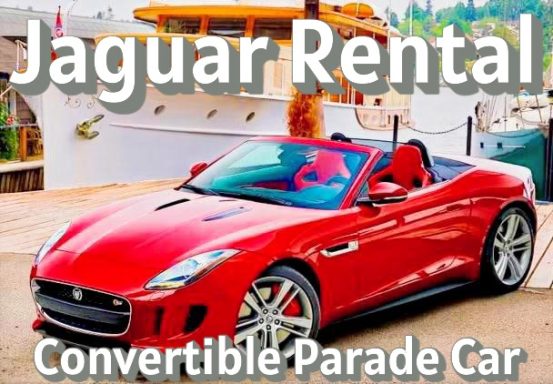 Red convertible Jaguar with a sleek design, parked near a boat.